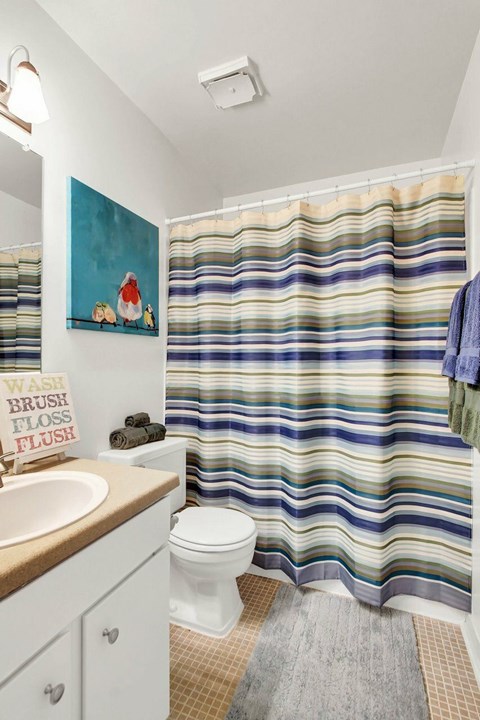 A bathroom with a striped shower curtain and a painting of Santa Claus on the wall.