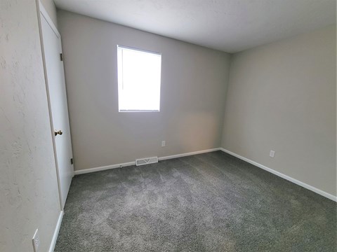 A room with a grey carpet and a window.