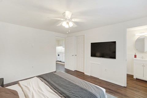A bedroom with a bed, a television, and a ceiling fan.