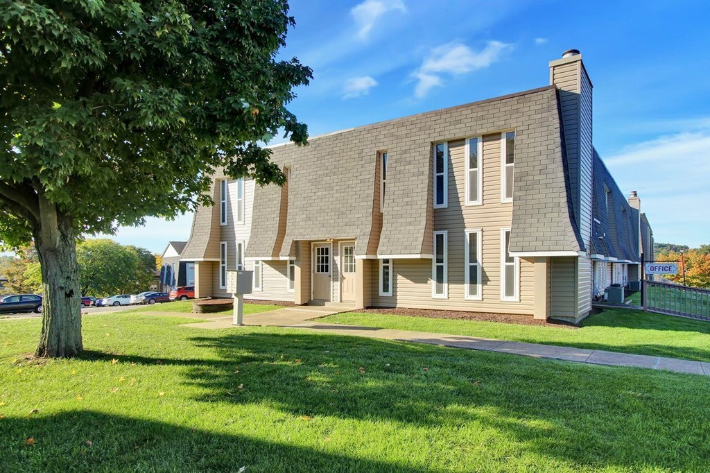 A modern house with a grey roof and a large tree in front.