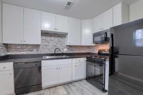 A kitchen with white cabinets and a black refrigerator.