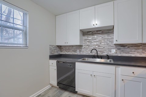 A kitchen with white cabinets and a stone backsplash.