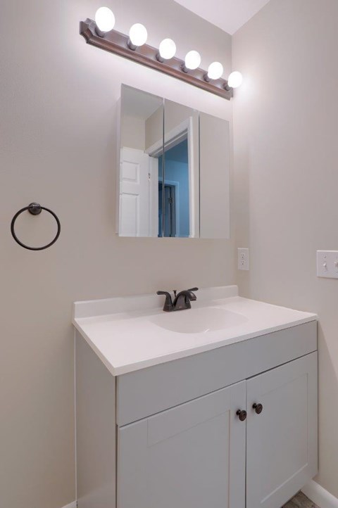 A bathroom vanity with a white countertop and a mirror with lights above it.