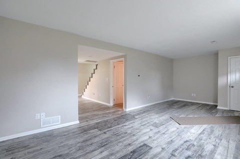 A room with a wooden floor and a staircase leading to another room.