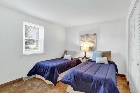 Two beds with blue bedspreads in a room with white walls.