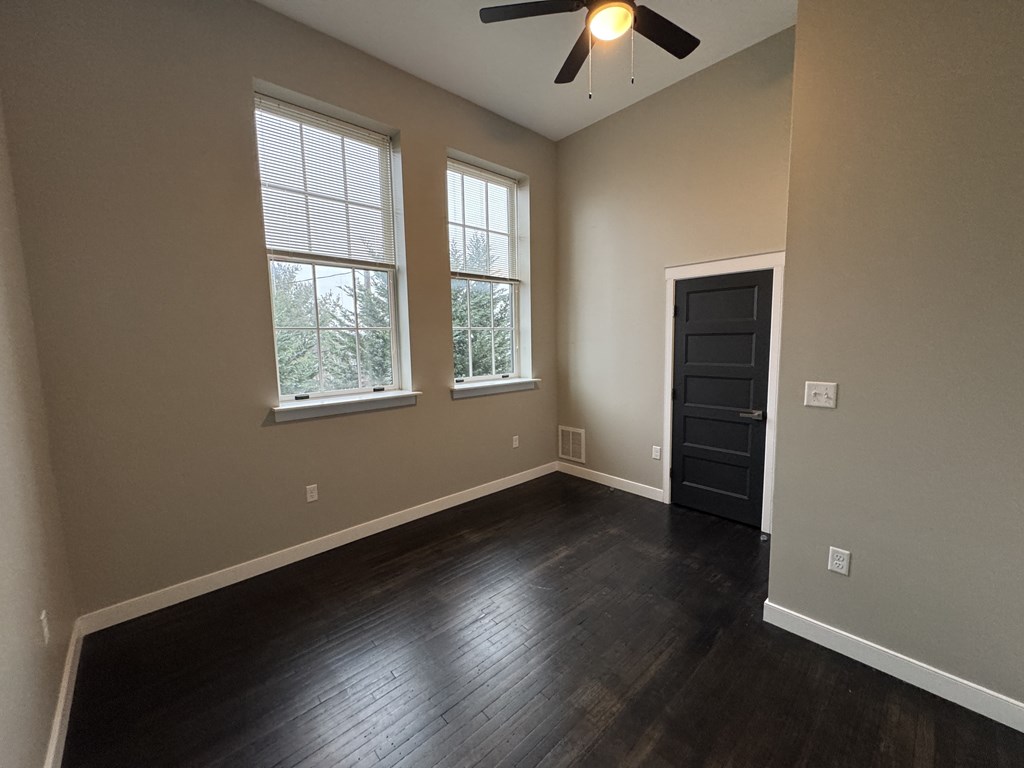 A room with a ceiling fan and two windows.