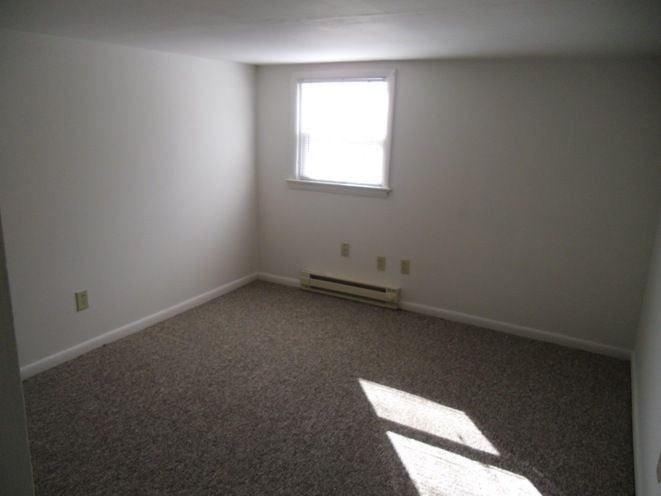 A room with a carpeted floor and a window letting in sunlight.