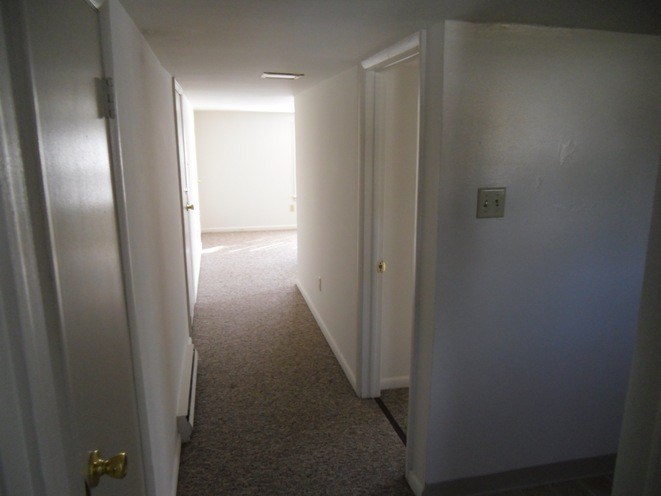 A hallway with a carpeted floor and white walls.