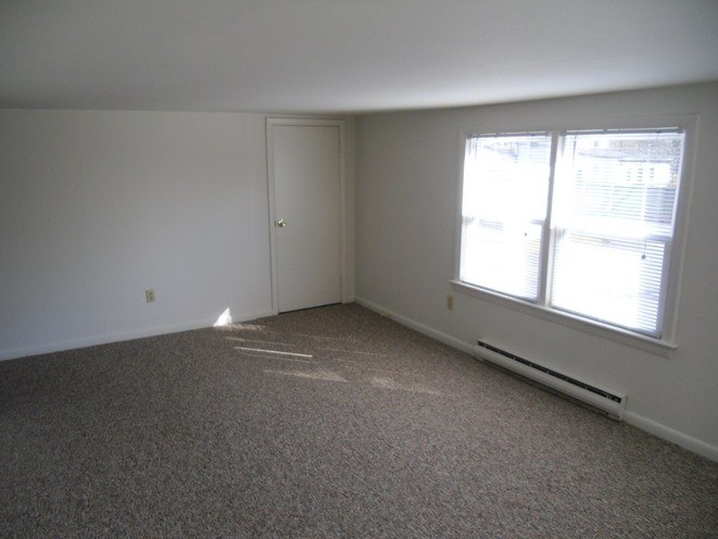 A room with a carpeted floor and a window letting in sunlight.