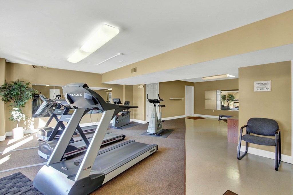A treadmill and a stationary bike are in a spacious room with a chair.