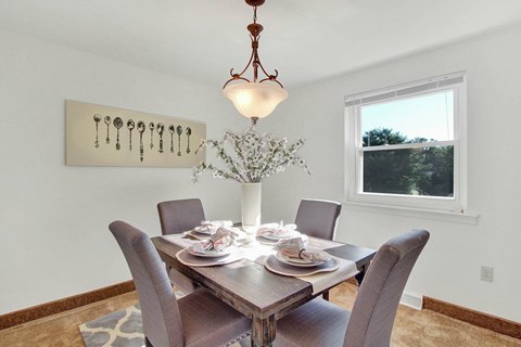 A dining room with a table set for four and a chandelier hanging from the ceiling.