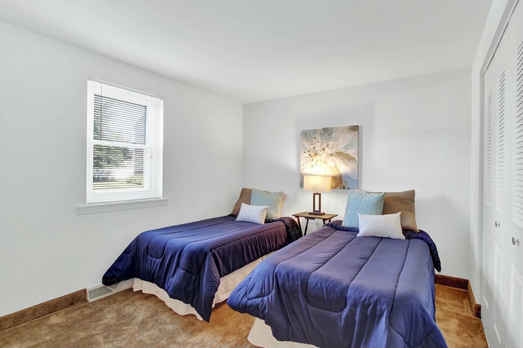 Two beds with blue bedspreads in a room with white walls.