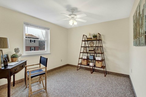 A room with a carpeted floor, a wooden chair, a wooden desk, and a window with a view of a house outside.