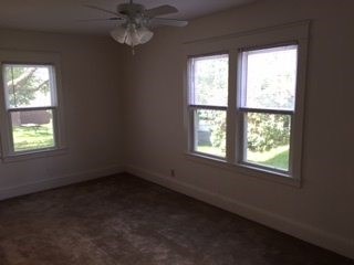 A room with a ceiling fan and three windows.