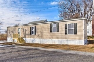 A beige mobile home with a white porch and a yellow chair.