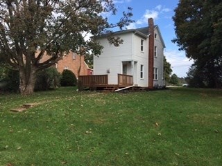 A white house with a brown door and windows is surrounded by trees.