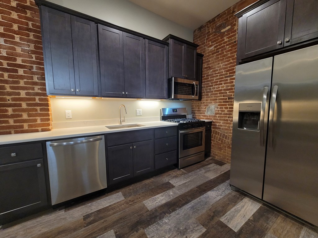 A kitchen with dark wood cabinets and a brick wall.