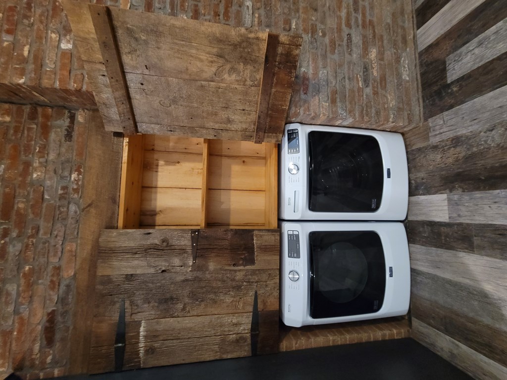 Two white microwaves are placed on a wooden shelf.