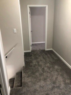 A hallway with a carpeted floor and a staircase.