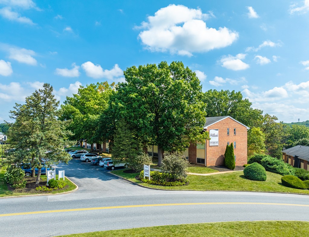 A building with a sign that says "Welcome" is surrounded by trees and a parking lot.