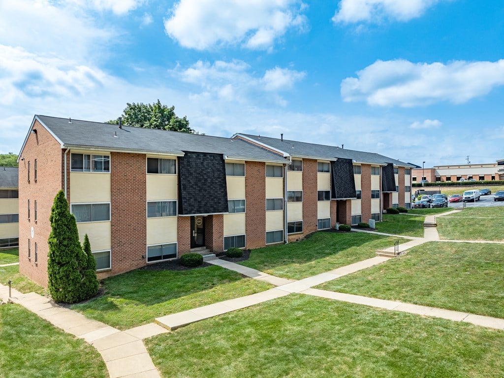 A row of apartment buildings with a tree and a walkway in front.