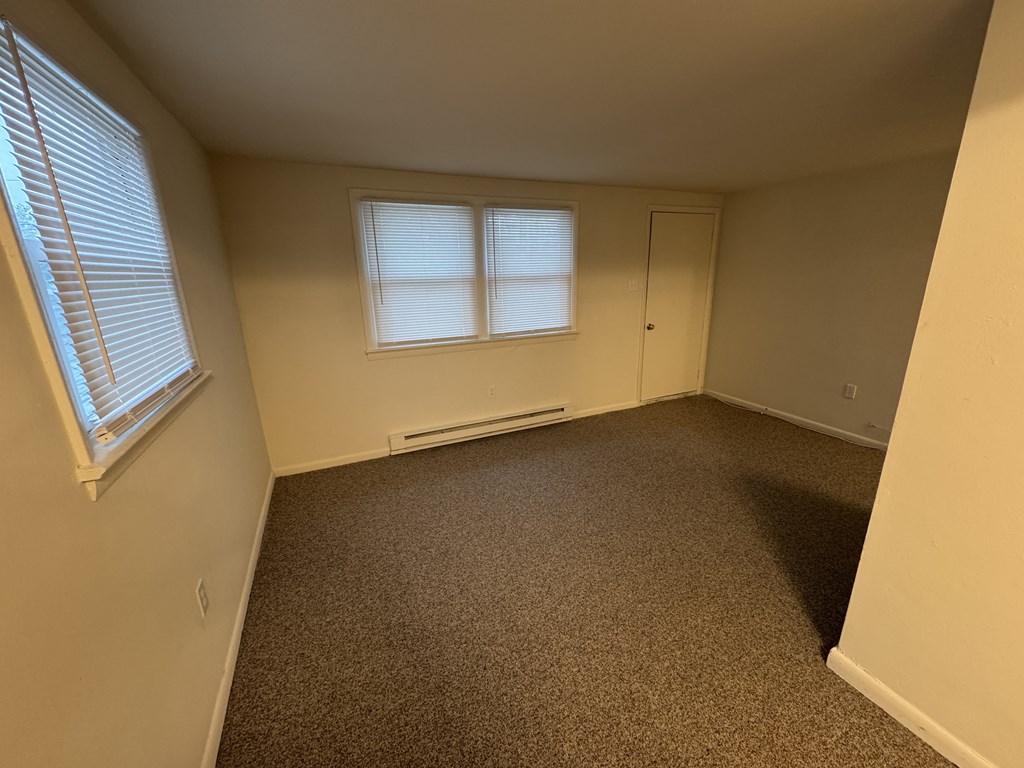A room with a carpeted floor, a window with blinds, and a door.