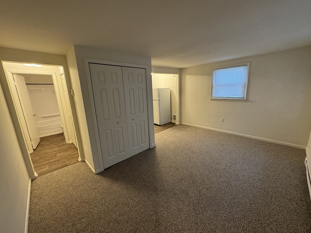 A room with a carpeted floor, a white door, and a window with blinds.