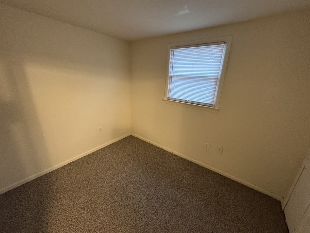 A room with a carpeted floor and a window with blinds.