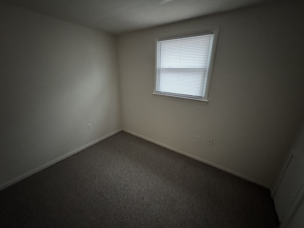 A room with a carpeted floor and a window with blinds.