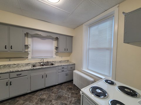 A kitchen with a white stove top oven and a window with blinds.