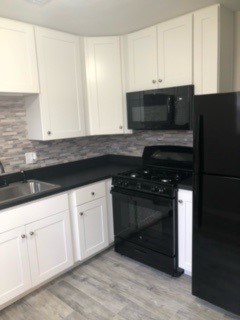 A black refrigerator sits next to a black stove in a kitchen with white cabinets.