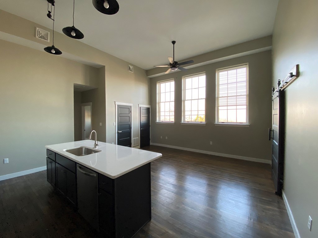 A kitchen with a sink and a countertop with a fan in the background.