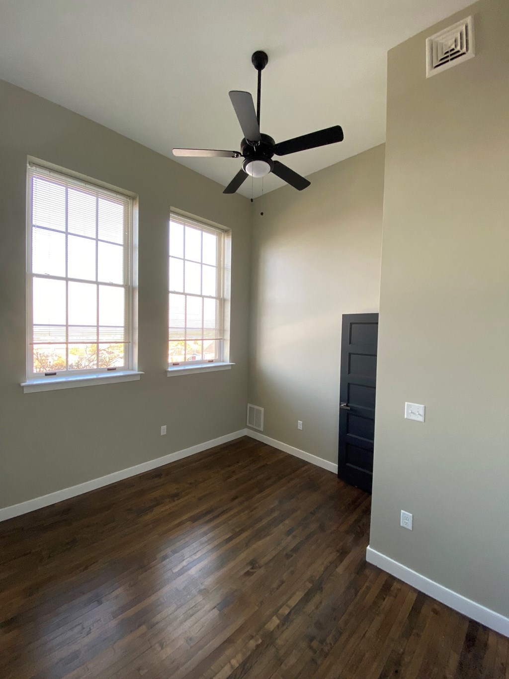 A room with a ceiling fan and two windows.