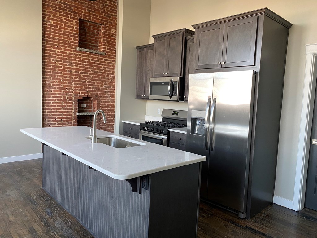 A kitchen with a brick wall and a refrigerator.
