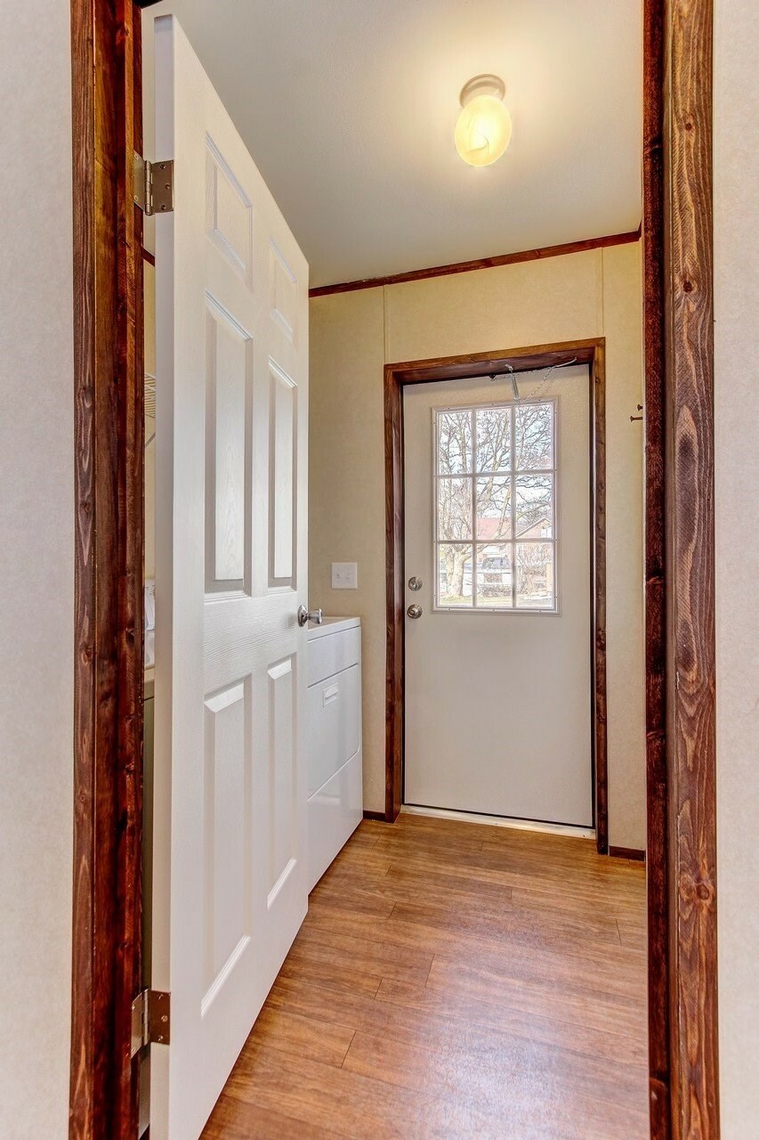 A white door is open to a hallway with wood floors and white walls.