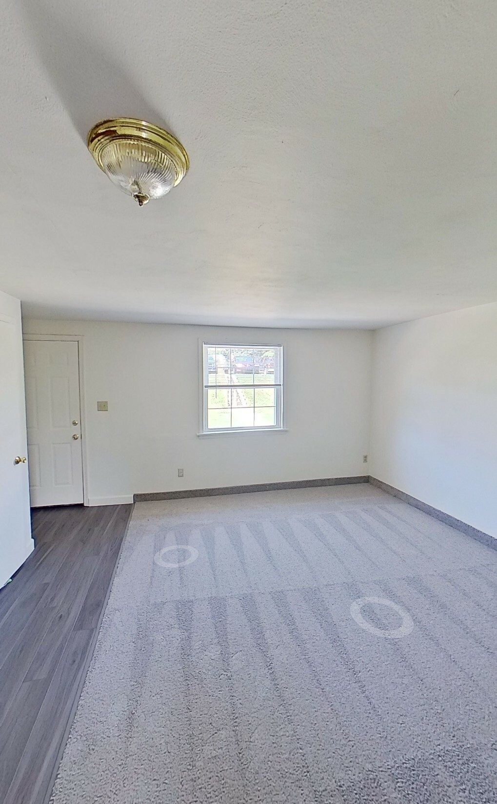 A room with a grey carpet and a window.