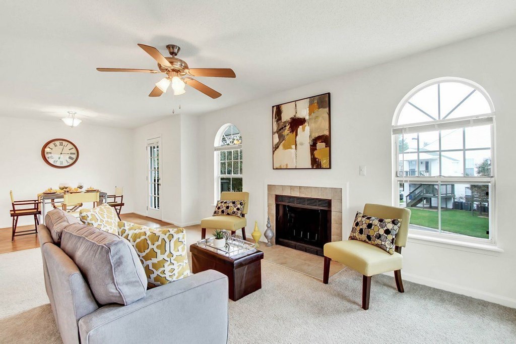 A living room with a grey couch, a yellow and white patterned sofa, a fireplace, and a ceiling fan.