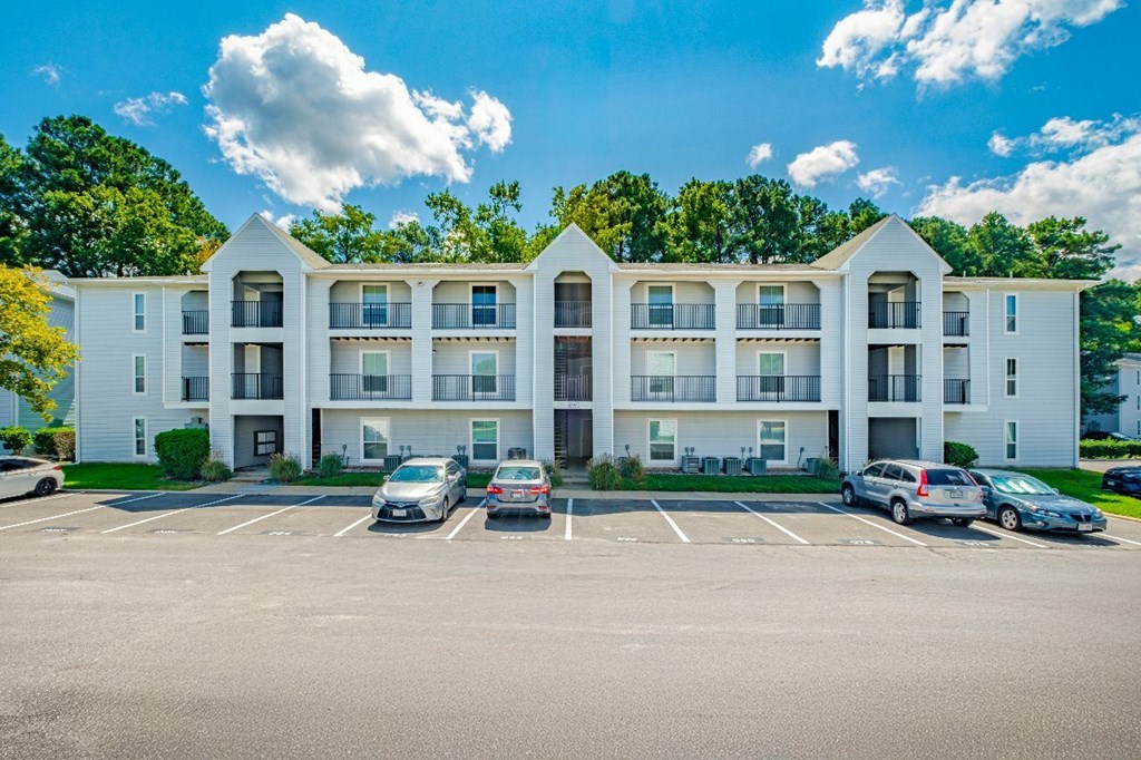 A large white apartment building with a parking lot in front.