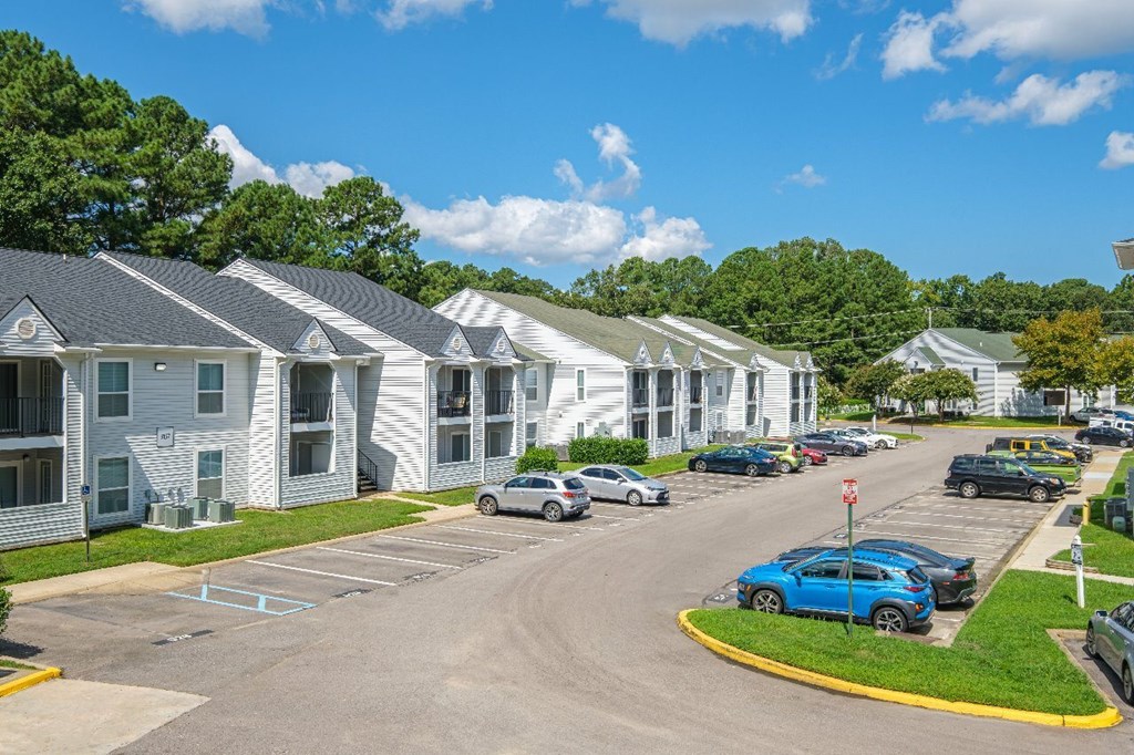 A blue car is parked in a parking lot in front of a white building.