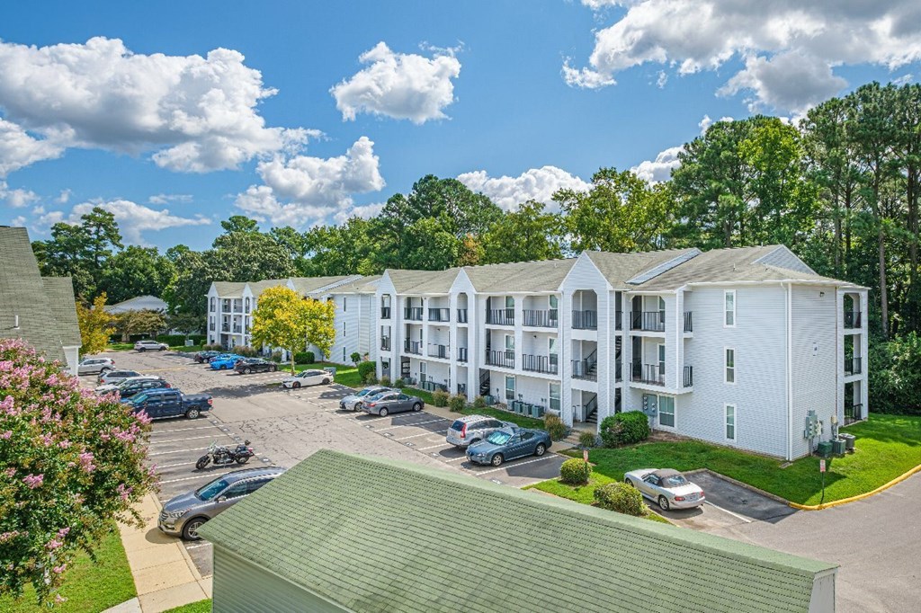 A white apartment complex with a green roof and cars parked in the parking lot.