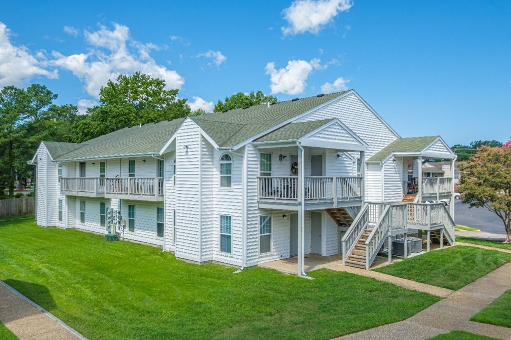 A white two story house with a green roof and a balcony on the second floor.