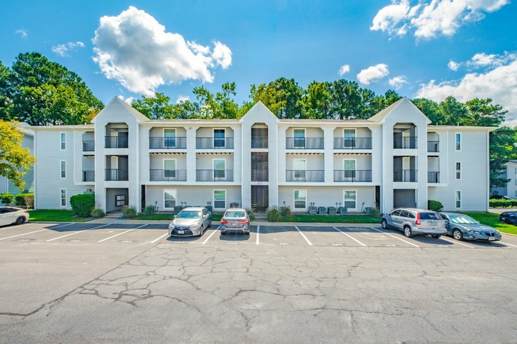 A large white apartment building with a parking lot in front.