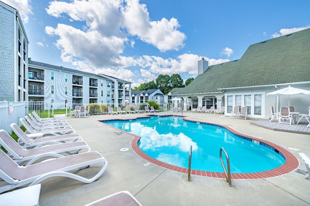 A pool surrounded by lounge chairs and apartment buildings.