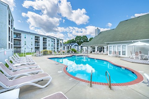 A pool surrounded by lounge chairs and apartment buildings.