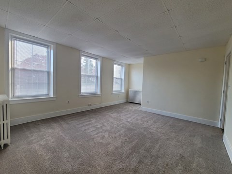 A room with carpeted floor and three windows.