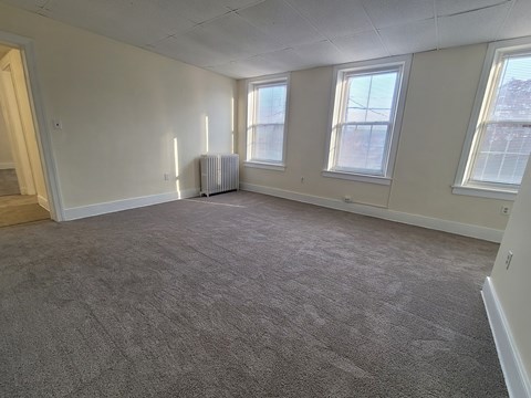 A room with grey carpet and three windows.