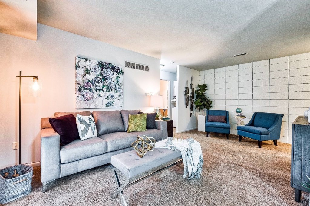 A living room with a grey couch and a white wall with a cross on it.