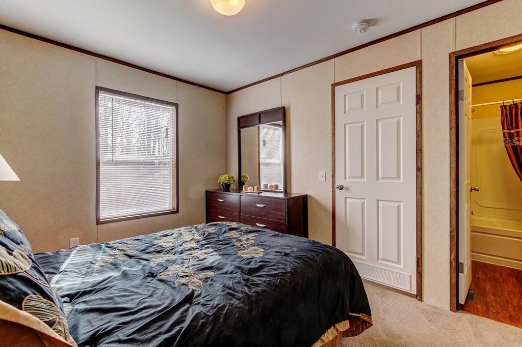 A bedroom with a bed, dresser, mirror, and window.