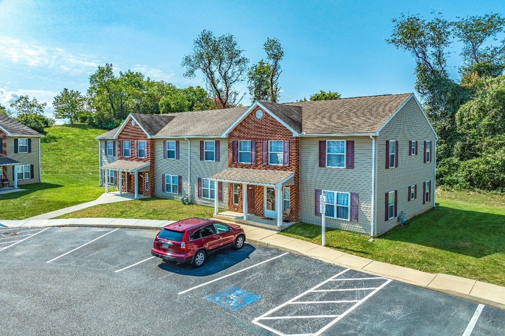 A red car is parked in a parking lot in front of a two-story building.