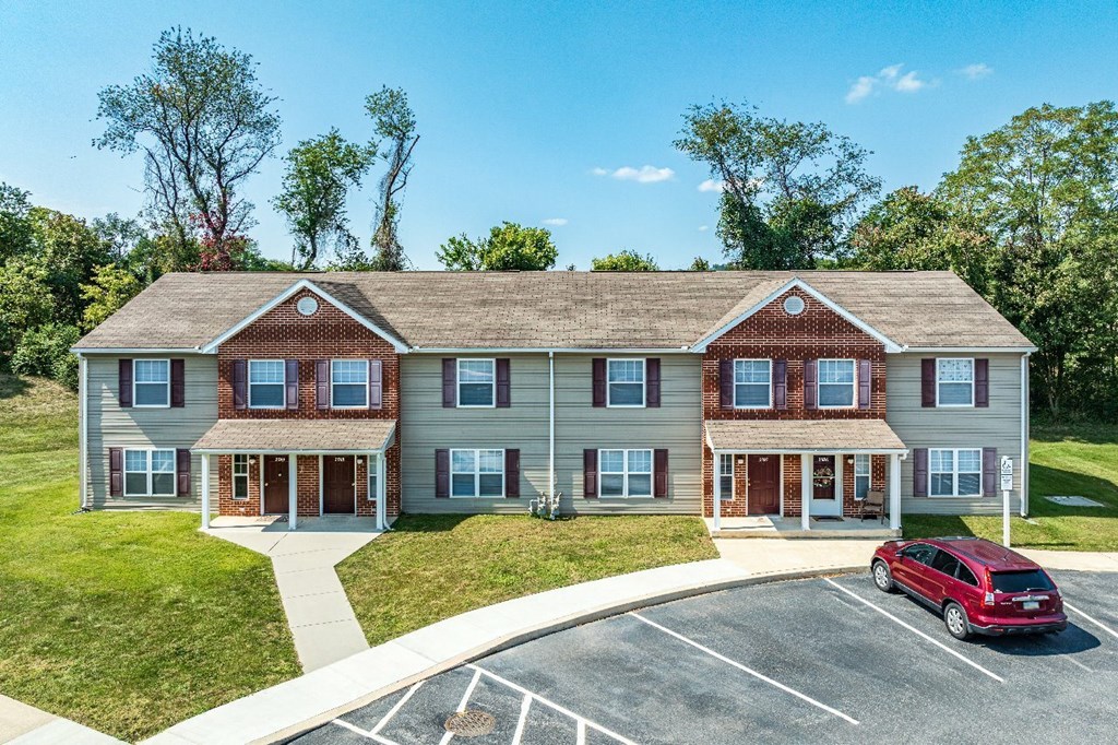 A red car is parked in the driveway of a two-story brick house.
